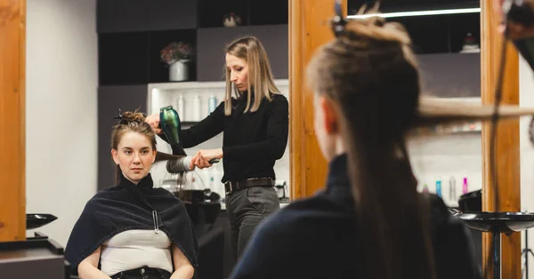 Maître femme coiffeur sèche les cheveux des filles avec un sèche-cheveux après le lavage dans un salon de beauté. — Photo