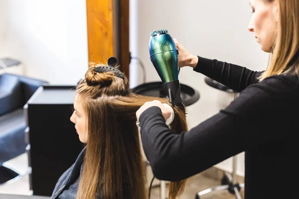 Master woman hairdresser dries the girls hair with a hairdryer and combs after washing in the beauty salon. — Stock Photo, Image