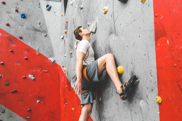 스턴트맨은 실내에 있는 인공 벽을 타고 가파른 바위 위를 기어오르고 있다. 극도의 스포츠와 둥그스름 한 개념 — 스톡 사진
