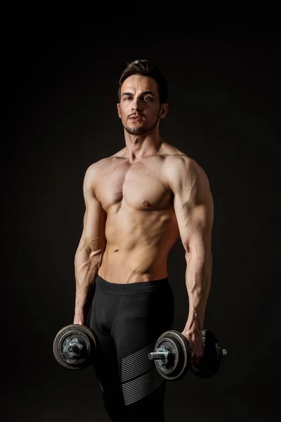 Retrato de un atleta musculoso atractivo con mancuernas sobre un fondo oscuro —  Fotos de Stock