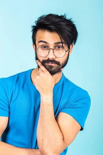 Ritratto emotivo di un bell'uomo indù con una maglietta blu su uno sfondo blu brillante, pensa a qualcosa — Foto Stock