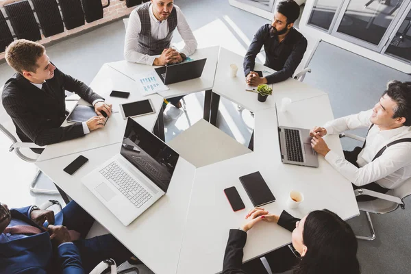 Grupo de jóvenes empresarios que trabajan y se comunican sentados en el escritorio de la oficina junto con sus colegas sentados. reunión de negocios. Escritorio vista superior. — Foto de Stock