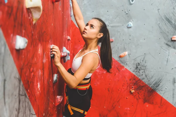 Deportiva escaladora ascendiendo sobre roca escarpada, escalando en pared artificial en interiores. Concepto de deportes extremos y bouldering — Foto de Stock