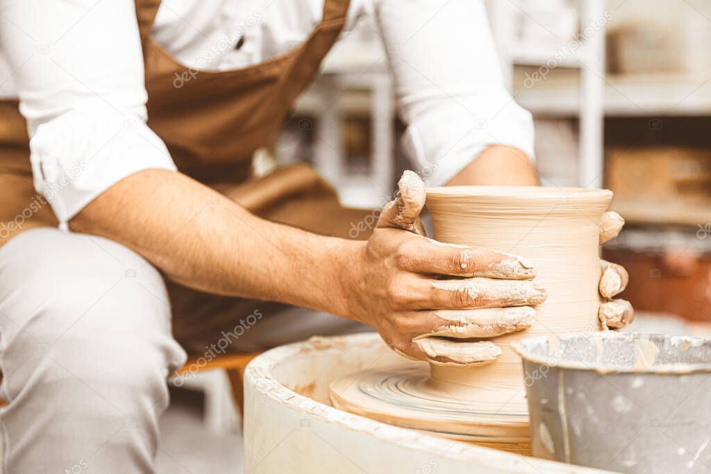 A young male potter works in his workshop on a potters wheel and makes clay products. Close-up of hands