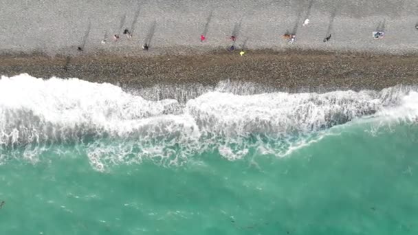 Вид з повітря на морське узбережжя. Люди ходять уздовж пляжу, а блакитні хвилі котиться на берег. Зверху вниз кадри безпілотника — стокове відео
