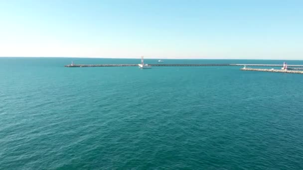 Flygfoto av ett vitt fartyg lämnar marinan, seglar längs vågbrytaren — Stockvideo