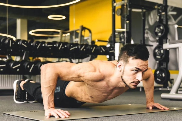 Jóképű fiatal sportos férfi testépítő meztelen felsőtesttel push-up gyakorlatot végez az edzőteremben — Stock Fotó