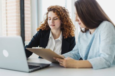 İki güzel genç bayan ofiste dizüstü bilgisayarla konuşup iş konuşuyorlar. bir proje üzerinde personel etkileşimi ve takım çalışması
