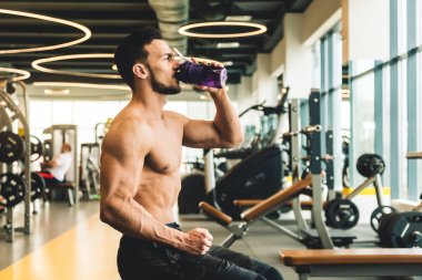 Egzersizler arasında dinlenirken su içen yakışıklı genç sporcu erkek vücut geliştirici.