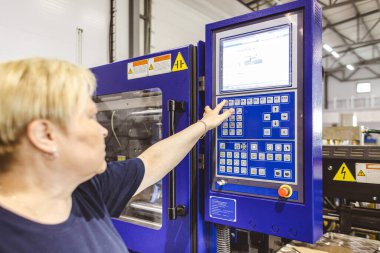 İşçi bir kadın düğmeye basıyor ve fabrikada otomatik üretim işlemi başlatıyor.