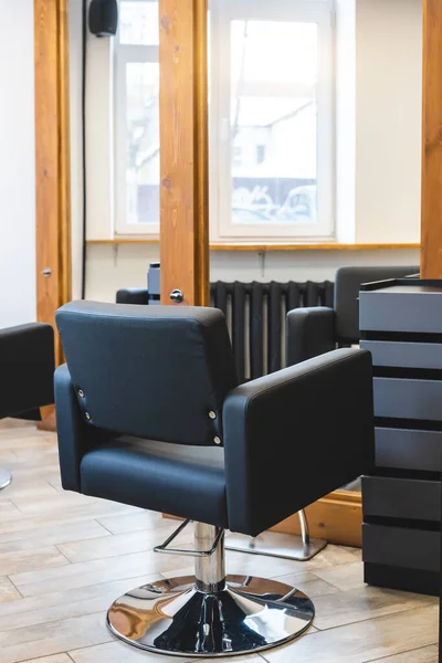 Beauty salon barbershop interior. Comfortable black leather armchairs in front of large panoramic mirrors in stylish wooden frames in a modern, cozy and bright room.