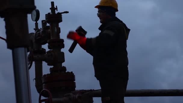 Pracovníci v montérkách a s tvrdými klobouky provádějí opravy a údržbu ropné vrty. Silueta na pozadí večerní oblohy — Stock video