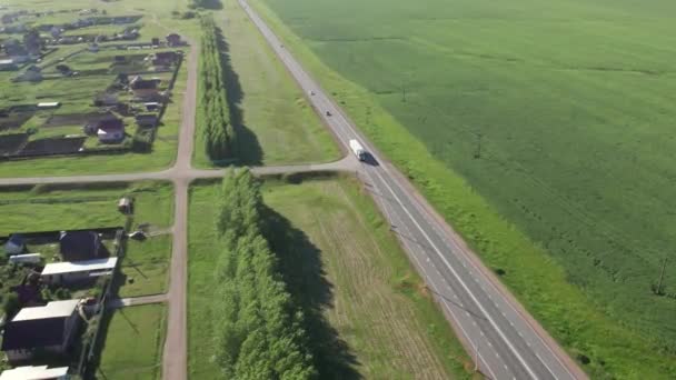 Вид з повітря на шосе з автомобілями і вантажівками, що проходять вздовж невеликих сіл, зелених полів і лугів . — стокове відео