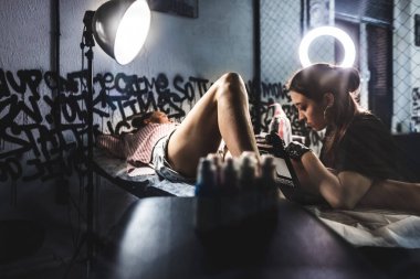 Bacağa yakın plan dövme çizimi. Kadın dövme sanatçısı bir sanat stüdyosunda özel bir makineyle çizim yapıyor.