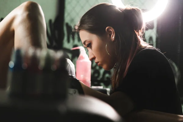 Profesional artista del tatuaje femenino hace un tatuaje en el estudio, de cerca. Fotografía oscura — Foto de Stock