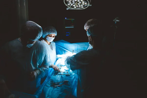 Ein internationales professionelles Team aus Chirurgen, Assistenten und Anästhesisten führt eine komplexe Operation an einem Patienten unter Vollnarkose durch. Dunkle atmosphärische Fotografie Thema in leiser Tonart. — Stockfoto