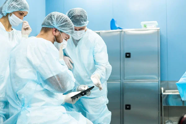 Üniformalı ve tıbbi maskeli bir doktor ekibi elektronik tablet üzerinde cerrahi bir plan inceliyor.