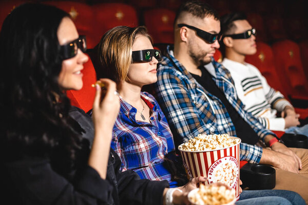 Friends are watching a movie in the cinema. People sit in the armchairs of the cinema and look at the screen with special glasses for 3D