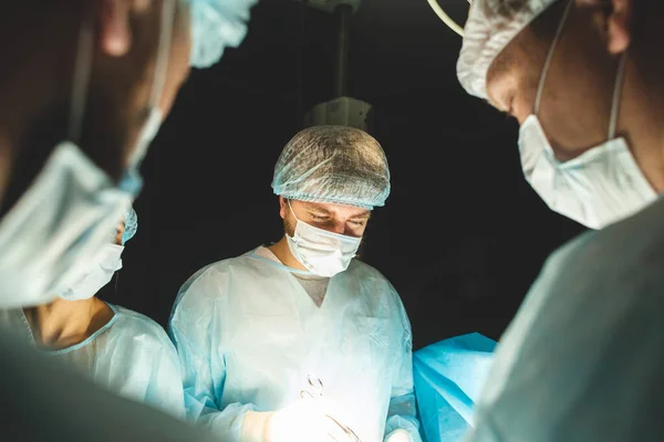 Une équipe internationale de chirurgiens, d'assistants et d'anesthésistes effectue une opération complexe sur un patient sous anesthésie générale. Thème de la photographie atmosphérique sombre en mode discret. — Photo