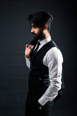 Siyah arka planda, siyah takım elbiseli, ceketini omzunun üstünde tutan yakışıklı, başarılı bir Hintlinin portresi.