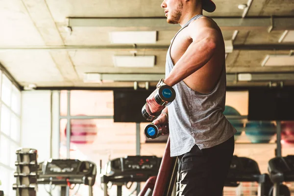 Atleta masculino jovem muscular executa exercícios com halteres. Treinamento de força no ginásio — Fotografia de Stock