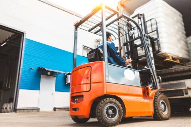 Forklift kullanan bir adam büyük bir depoda çalışır ve bir çanta dolusu hammaddeyi boşaltır.