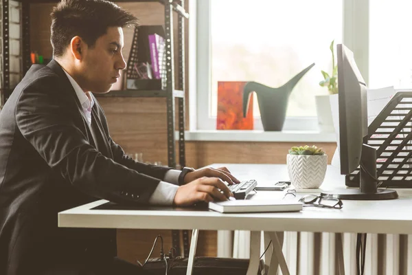 Jeune employé de bureau assis au bureau, utilisant l'ordinateur. Deux hommes d'affaires parlent — Photo