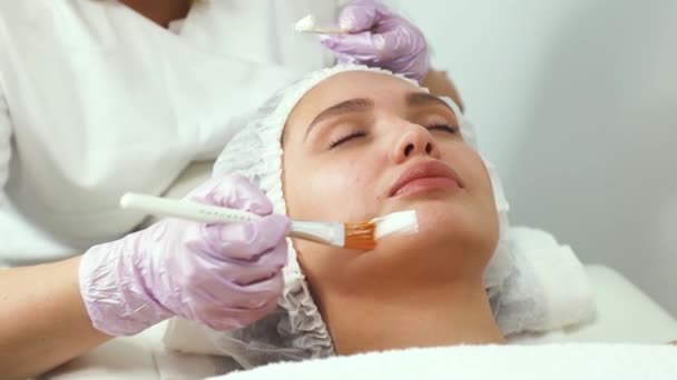 Soins et protection du visage. Une jeune femme à un rendez-vous d'esthéticienne. Le spécialiste applique un masque crème sur le visage — Video