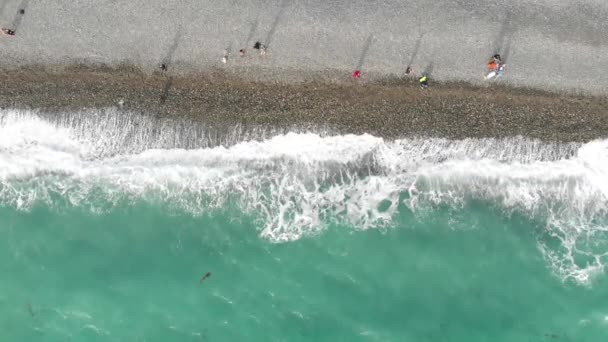 Vista aérea da costa marítima. As pessoas caminham ao longo da praia e ondas azuis rolam para a costa. Imagens de drones de cima para baixo — Vídeo de Stock