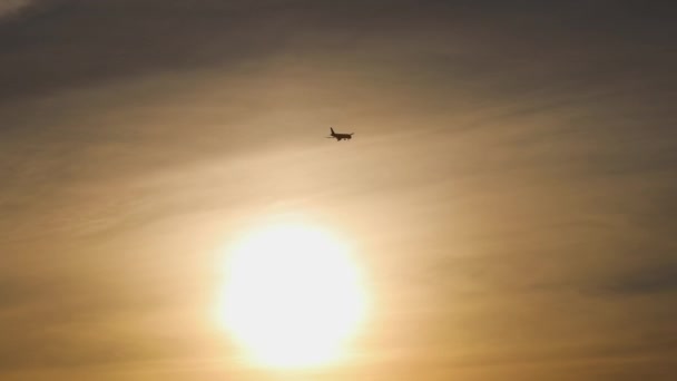 Silueta de un avión de pasajeros aterrizando al atardecer sobre el telón de fondo de un enorme sol naranja — Vídeo de stock