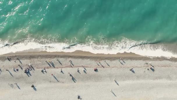 Luchtfoto van de zeekust. Mensen lopen langs het strand en azuurblauwe golven rollen de kust op. Top-down drone beelden — Stockvideo