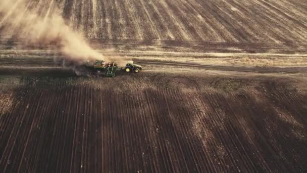 El dron 4K que dispara desde arriba del tractor trabaja en el campo y araña el suelo, levantando polvo. Preparación y cultivo del suelo para la próxima temporada de cosecha — Vídeo de stock