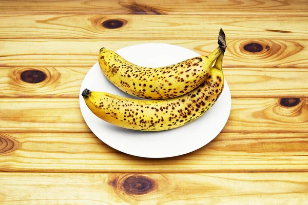 Ripe Speckled Bananas White Plate Top Angle View Wooden Table — Zdjęcie stockowe