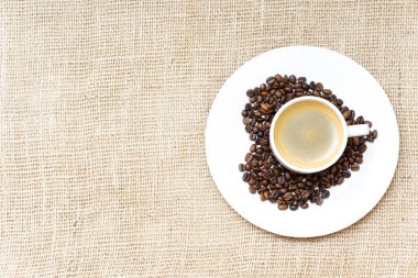 Kavrulmuş kahve çekirdeklerinden yapılmış bir kalp sembolü ve çuval bezinde bir kahve fincanı.