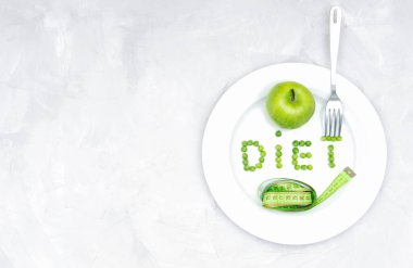 Büyük beyaz bir tabakta taze yeşil bir elma, yumuşak bir mezura ve beton bir masanın çatalından oluşan bezelyelerden oluşan bir diyet. Sağlıklı yaşam tarzı, kilo kaybı ve diyet konsepti.