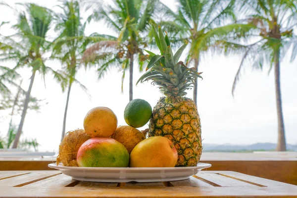 一盘异国情调的水果放在木制桌子上 背景上有棕榈树 — 图库照片