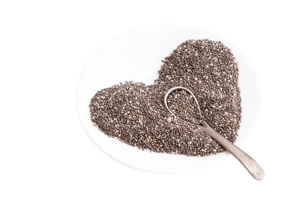 Chia tohumlarından yapılmış kalp sembolü ve beyaz bir tabakta izole edilmiş küçük bir çelik kaşık.