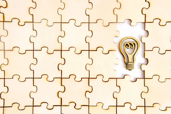Wooden jigsaw puzzle background with two missing pieces and a small flat steel copy of a light bulb