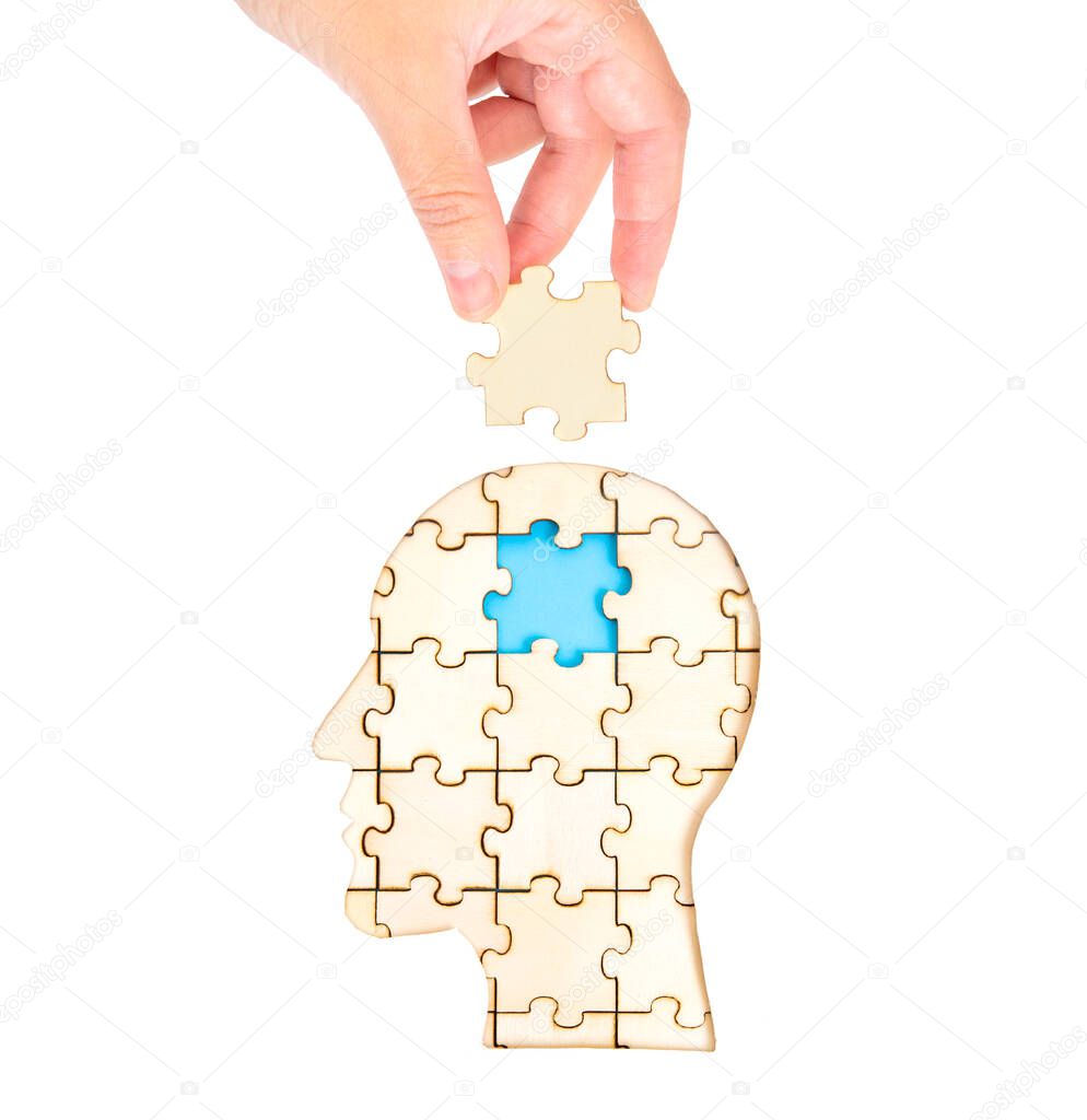 Female hand placing the missing brain piece of the jigsaw puzzle forming a human head isolated on white. Mental treatment and therapy concept.