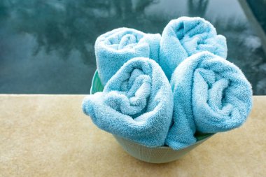 Havuzun yanında dört rulo yumuşak havlu olan plastik sepet.