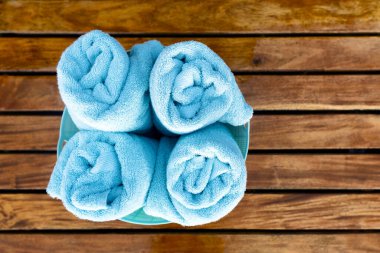 Tahta bir arka planda plastik bir sepette yuvarlanmış dört yumuşak havlunun üst görüntüsü.