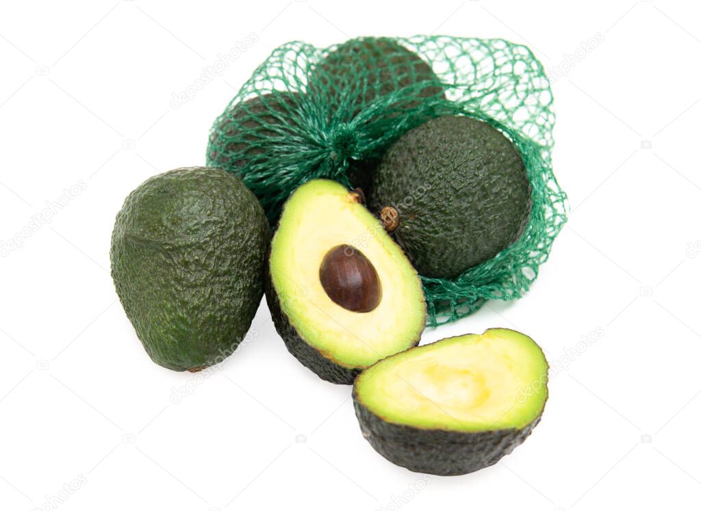 Group of fresh avocados in a green mesh bag isolated on white. One avocado fruit is cut open.