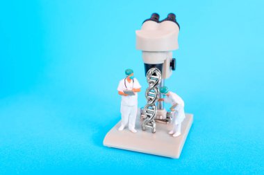 Metalik DNA sarmalını mikroskop altında inceleyen minyatür bilim insanlarının yakından görüntüsü moleküler biyoloji araştırmalarının karmaşık detaylarını vurguluyor..