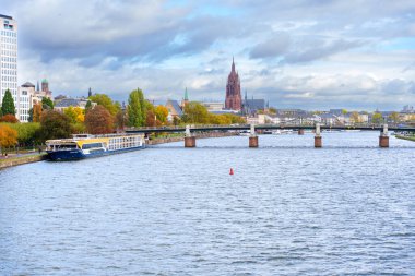 Frankfurt, Almanya - 21 Ekim 2025: Frankfurt 'un Main River' ı tarihi Eiserner Steg, ikonik Katedral ve dinamik bir gökyüzü altında modern şehir silueti içeren pitoresk bir manzara sunuyor..
