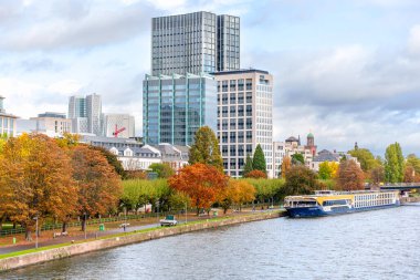 Frankfurt, Almanya - 21 Ekim 2025: Frankfurt 'un Main Riverfront şehri tarihi mimari, canlı sonbahar ağaçları ve demirlemiş bir nehir turu teknesiyle birleştirilmiş modern gökdelenleri sergilemektedir..