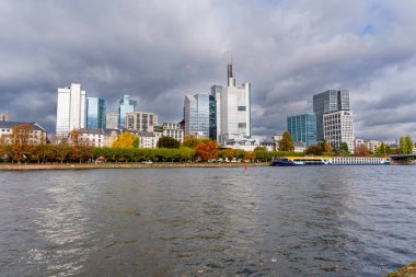 Frankfurt, Almanya - 21 Ekim 2025: Frankfurt Main 'in ikonik finans bölgesi ve nehir kıyısında bir tur teknesiyle dramatik bir sonbahar gökyüzü altında tarihi nehir kenarı mimarisi yükselişi.
