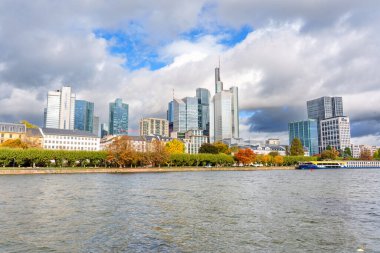 Frankfurt, Almanya - 21 Ekim 2025: Frankfurt am Main 'in ikonik şehir manzarası, ana nehir boyunca uzanan sonbahar ağaçları ile çevrili gökdelenmiş gökdelenler ve geleneksel mimariye sahiptir..