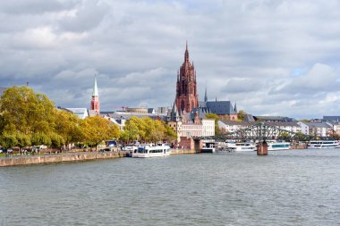 Frankfurt, Almanya - 21 Ekim 2025: Frankfurt 'un ana nehrinin panoramik perspektifi tarihi mimarisi, Eiserner Steg köprüsü ve dinamik kentsel kentsel manzarayı tanımlayan canlı sonbahar yeşilliği.