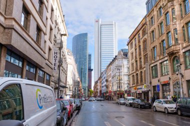 Frankfurt, Germany - October 21, 2025: Urban street in Frankfurt, featuring a diverse architectural landscape from traditional facades to contemporary high-rises, with parked vehicles.