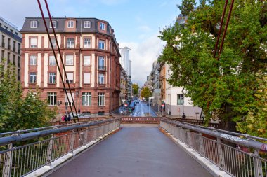 Frankfurt, Germany - October 21, 2025: Frankfurt's cityscape from a bridge, revealing historic architecture, a distant modern skyscraper, and lush green trees framing an urban street.